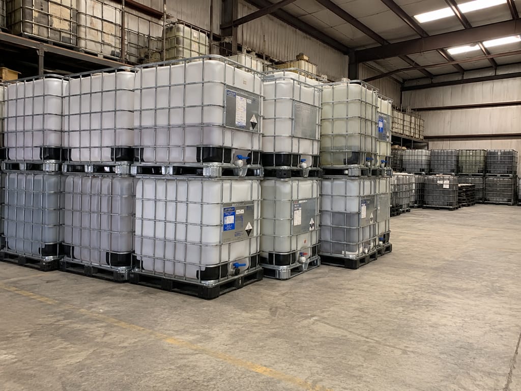 Warehouse interior with double-stacked IBC totes carrying hazard placards on steel racking